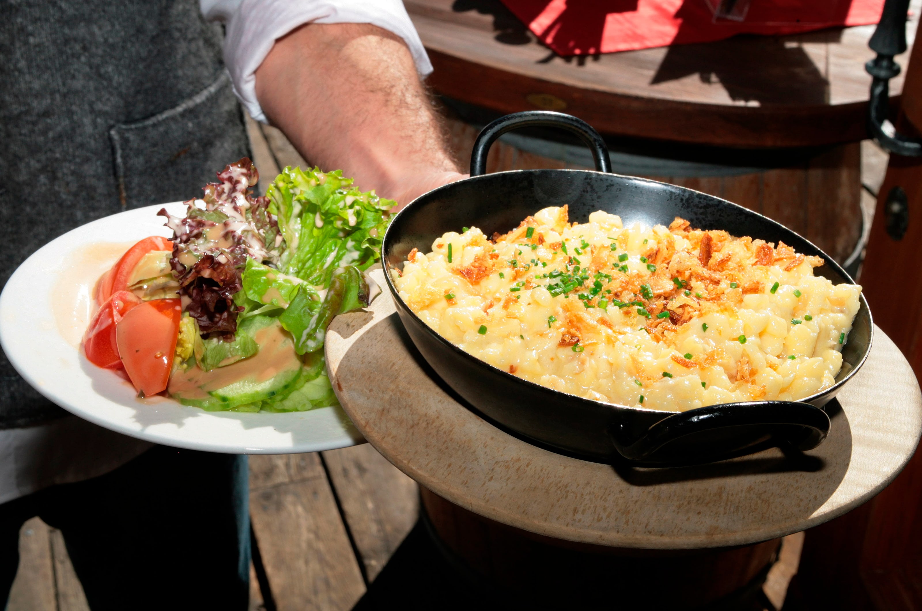 Eine Pfanne mit Käsespätzle und Röstzwiebeln, daneben ein Teller gemischter Salat