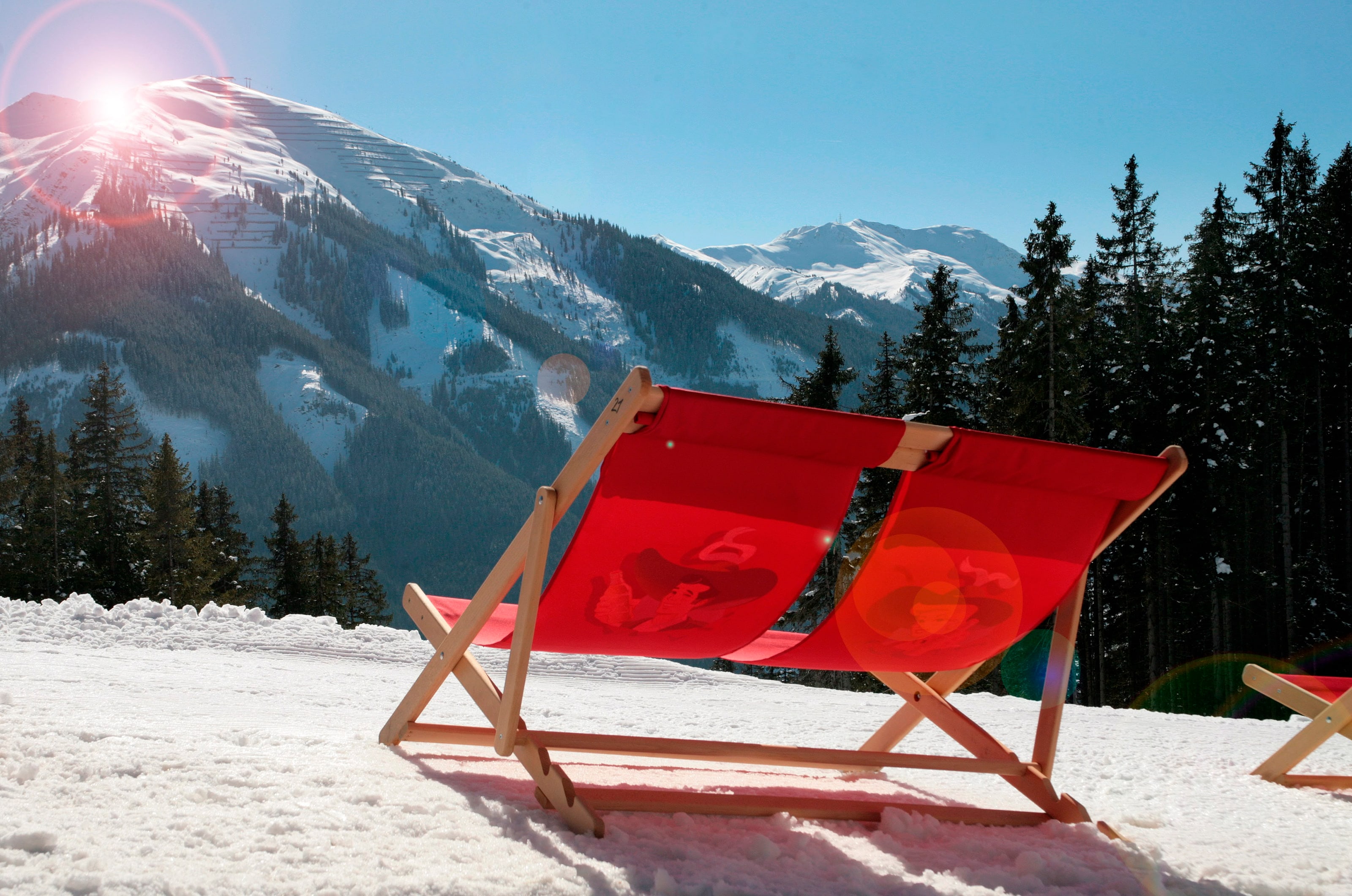 Rote Liegestühle im Schnee vor der Hütte, dahinter das verschneite Bergpanorama